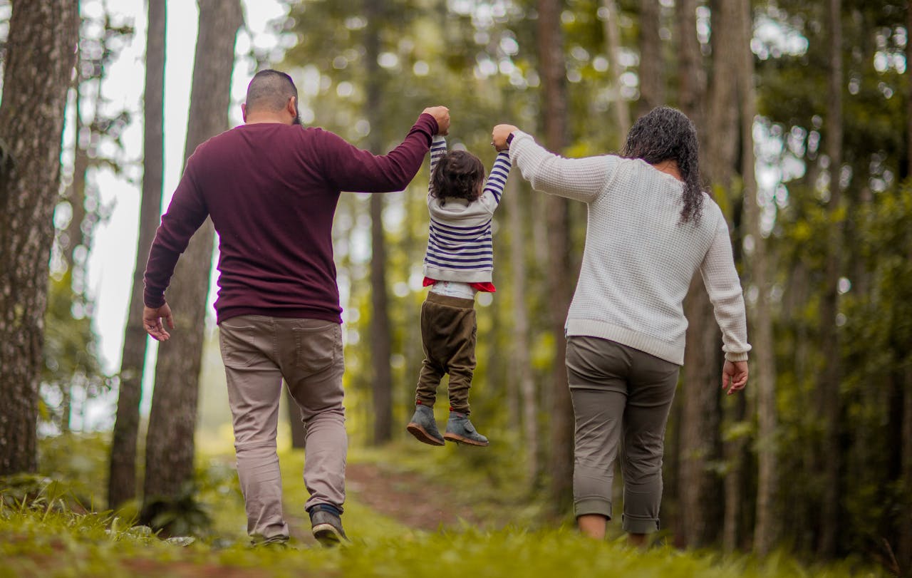 A happy family walking through a forest, lifting their child playfully outdoors.